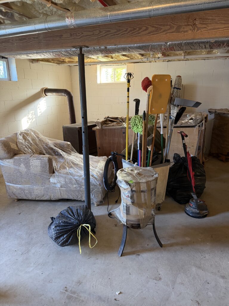 Before basement junk removal in Blairsville, Georgia, showing a sofa, furniture, cleaning equipment, and bags awaiting removal by Appalachian Junk Removal, LLC.