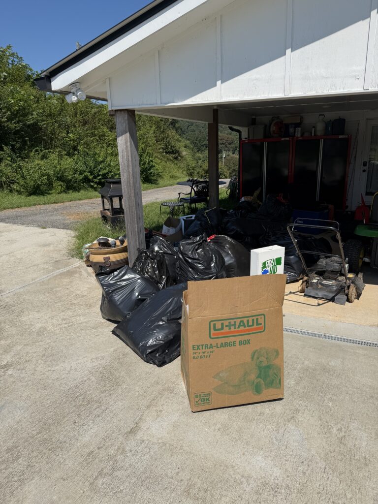 Before carport junk removal in Blairsville, Georgia, showing black trash bags, cardboard boxes, and unwanted items awaiting pickup by Appalachian Junk Removal, LLC.